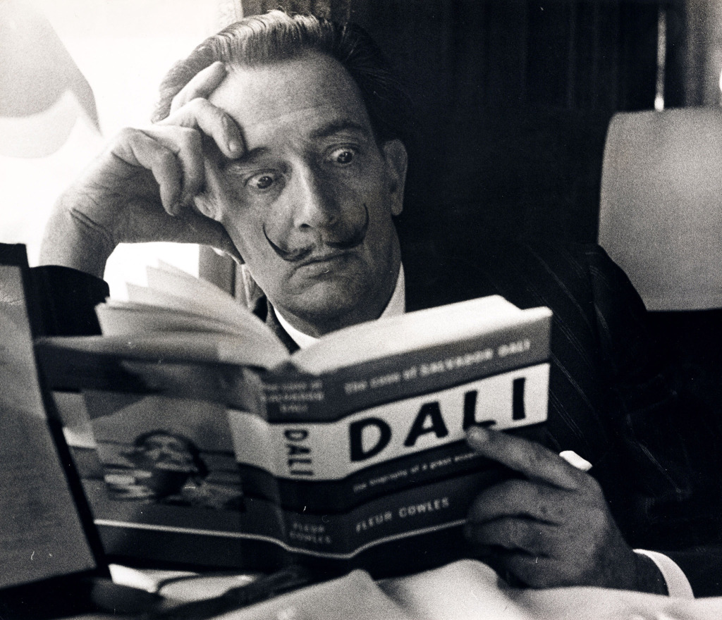 Salvador Dali reading his biography, 6 May, 1959 Black and white photograph of Salvador Dali reading his biography on the train, 1959.
