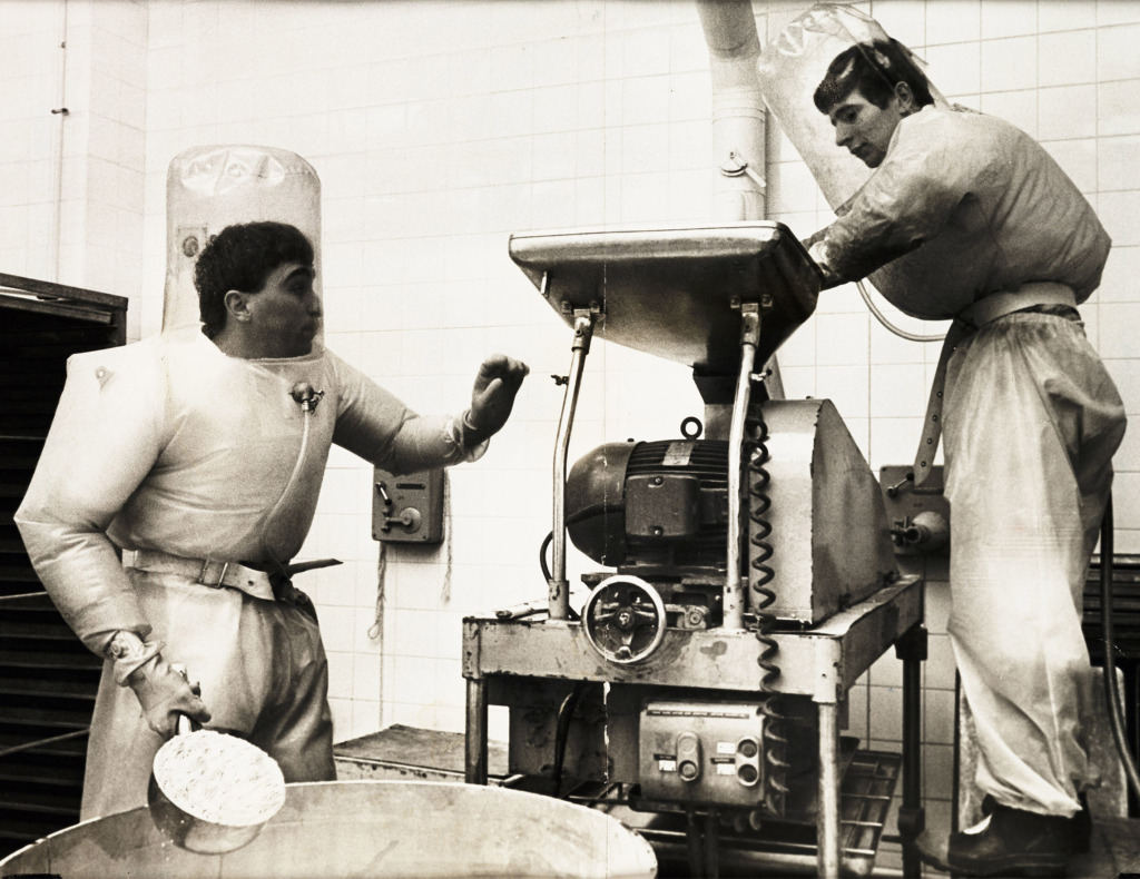 'The Pill', 1968 Black and white sepia photograph of two workers wearing inflated PPE suits in the wet granulating room at a pharmaceutical factory.